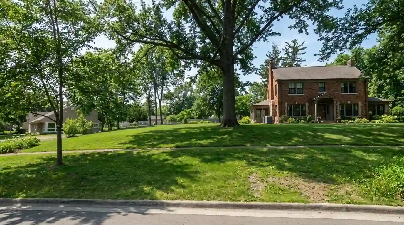 A two-story 1920s brick period home in Wildwood Park, Fort Wayne, Indiana, on a hot July afternoon, deep front lawn, tall shade trees, condenser beside the porch